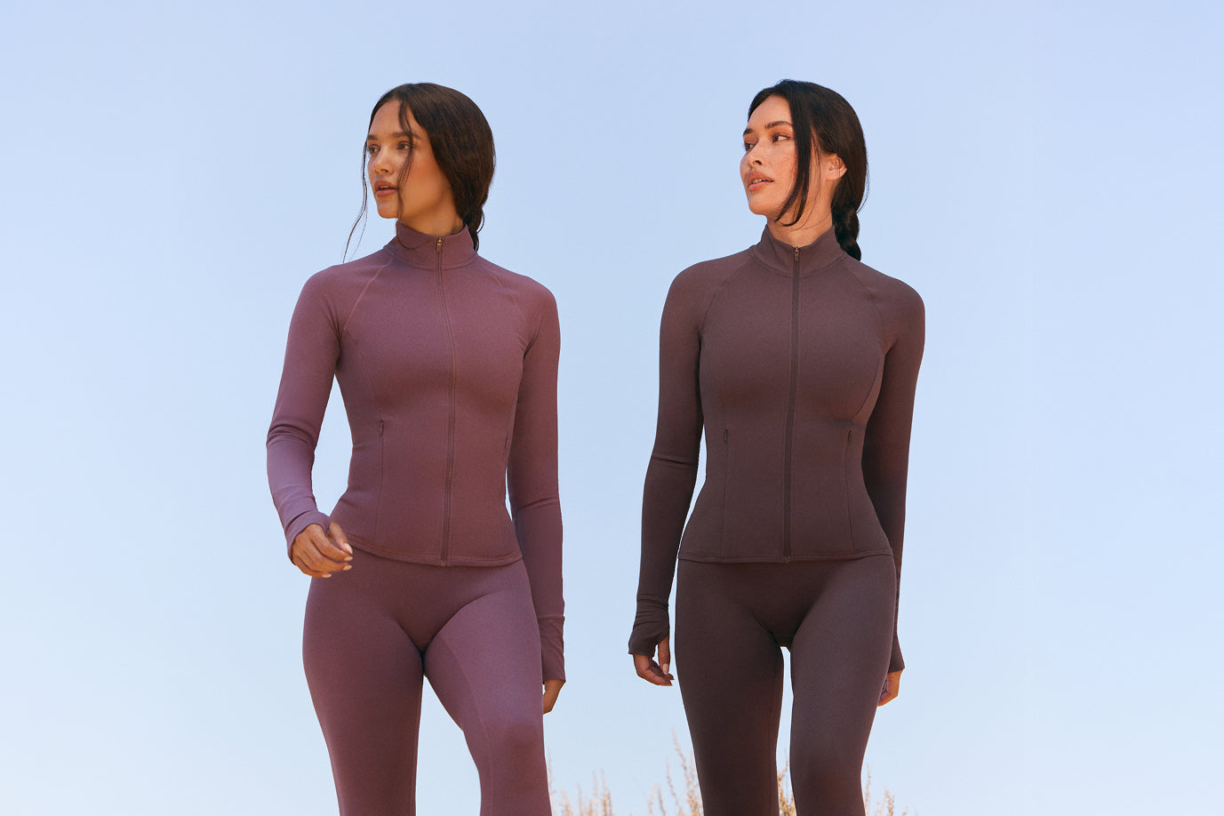 Two models are shown from the legs up wearing matching long-sleeved tops and leggings in Vintage Purple and Dark Umber Brown. 